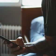 Dłoń trzymająca smartfon, z widocznym tatuażem na przedramieniu.