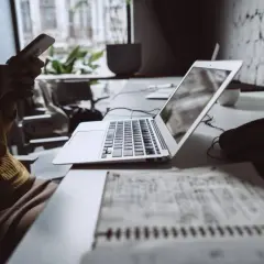 Kobieta z telefonem w ręku przy biurku z laptopem i notatkami.