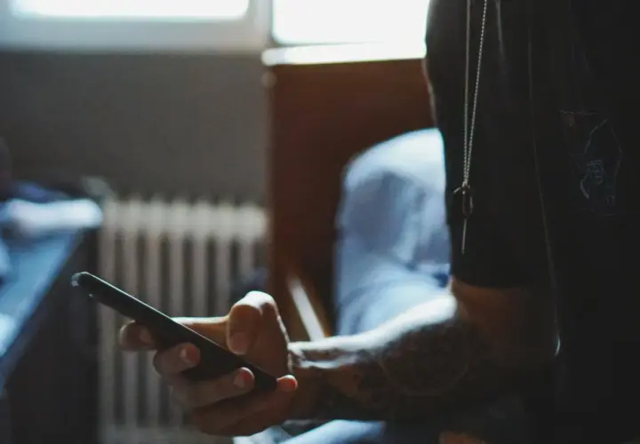 Dłoń trzymająca smartfon, z widocznym tatuażem na przedramieniu.