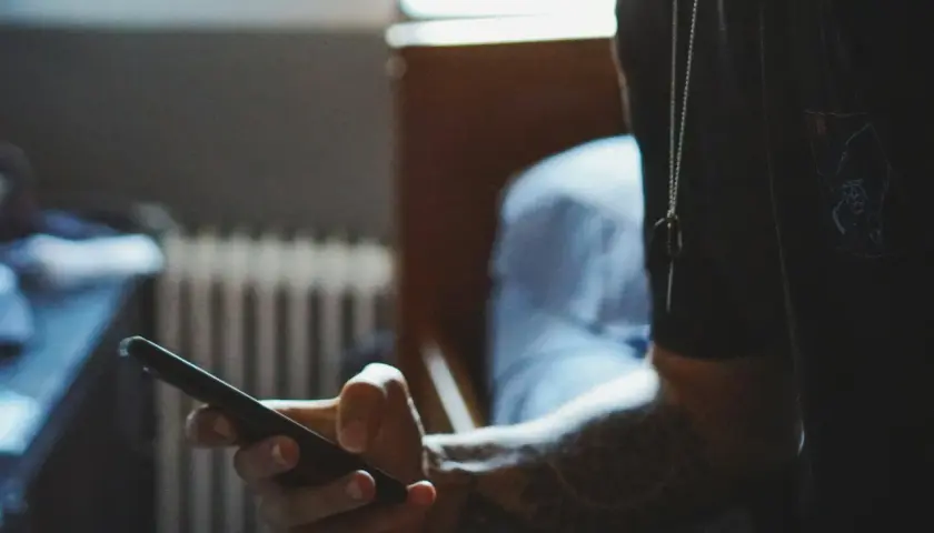 Dłoń trzymająca smartfon, z widocznym tatuażem na przedramieniu.