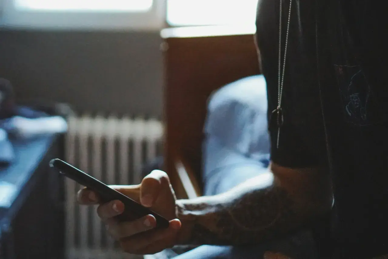 Dłoń trzymająca smartfon, z widocznym tatuażem na przedramieniu.